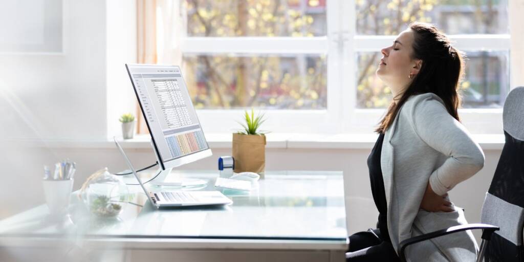 Personne assise à un bureau, manifestant une douleur lombaire due à une mauvaise posture prolongée.